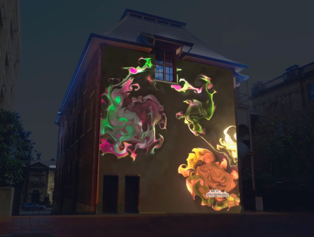 A photo of the former printery building. A colorful, watery image is projected onto one of its walls.